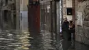 Seorang pria membawa hewan peliharaannya di depan rumahnya melalui daerah banjir di dekat Sungai Ebro di Tudela, Spanyol utara (12/12/2021). Hujan deras menyebabkan banjir di Spanyol utara. (AP Photo/Alvaro Barrientos)