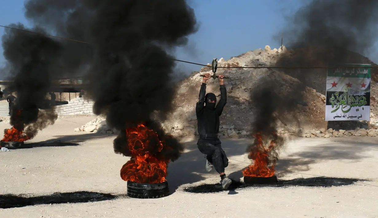 Aksi pasukan pemberontak melintasi kobaran api sat mengikuti latihan militer di provinsi Idlib, Suriah, (27/10). (REUTERS/Ammar Abdullah)