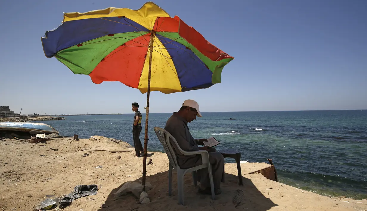 Seorang pria membaca Al-Quran bulan suci Ramadan di pantai Kota Gaza, Palestina, Jumat (1/5/2020). (MOHAMMED ABED/AFP)