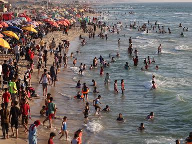 Warga Palestina berkumpul di pantai Beit Lahia di Jalur Gaza utara saat para siswa memulai liburan musim panas mereka pada 3 Juni 2022. Sejumlah warga menikmati musim panas dengan berenang dan bermain air di pantai. (MOHAMMED ABED / AFP)