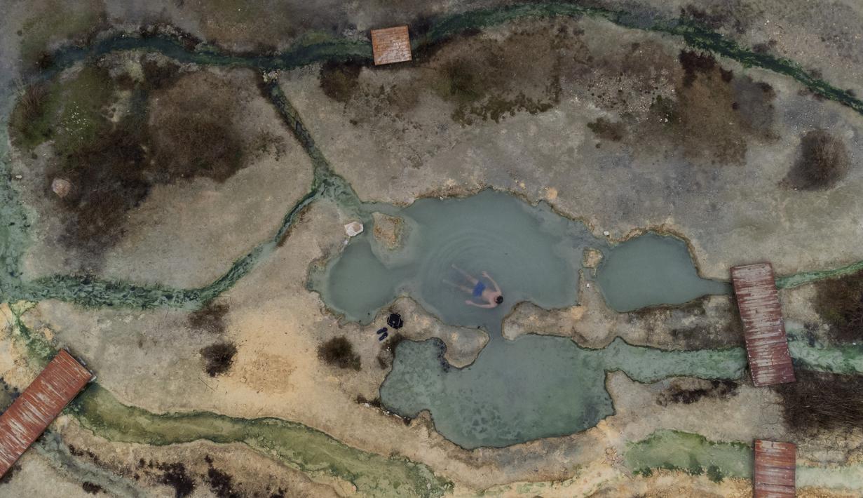 Seorang pria menikmati air panas di mata air mineral alami pada hari musim dingin di dekat desa Rupite, Bulgaria (2/2/2022). Penduduk setempat percaya bahwa air mineral menyembuhkan banyak penyakit dan gangguan. (AFP/Nikolay Doychinov)