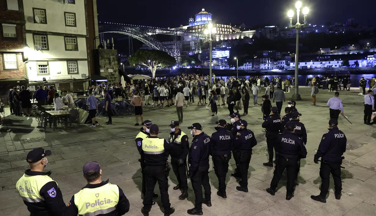 Petugas polisi mengawasi pendukung Manchester City yang berkumpul di tepi sungai Douro di Porto, Portugal (28/5/2021).  Manchester City akan bertanding melawan Chelsea pada babak final Liga Champions pada Sabtu malam atau Minggu (30/5/2021) dini hari. (AP Photo/Luis Vieira)