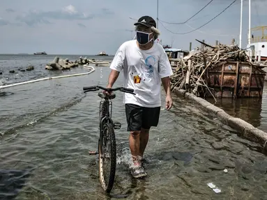 Warga menuntun sepeda saat melintasi banjir rob di Pelabuhan Kali Adem, Muara Angke, Jakarta, Kamis (22/10/2020). Banjir akibat air pasang dengan ketinggian mencapai 30 cm tersebut telah merendam kawasan Pelabuhan Kali Adem dan sudah berlangsung selama lima hari. (merdeka.com/Iqbal S. Nugroho)