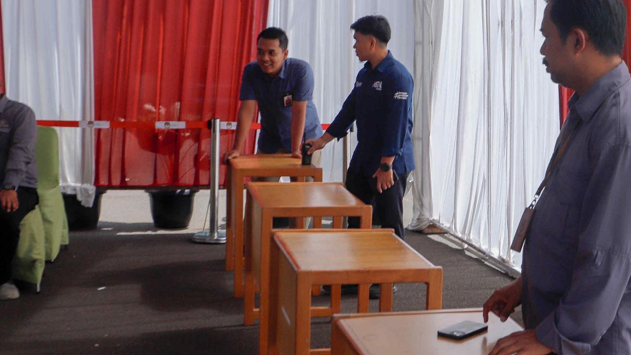 Beberapa petugas tampak sedang berdiri di depan 4 meja cokelat yang menjadi tempat untuk menaruh bilik suara. Foto: liputan6.com / Herman Zakharia<br>