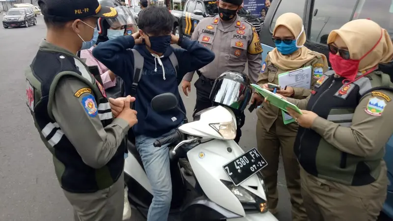Petugas gabungan satpol pp, tni-polri menghentikan salah satu warga yang tidak menggunakan masker, dalam razia gabungan hari pertama penerapan aturan ketat penggunaan masker di Garut, Jawa Barat.