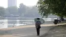Seorang wanita mengenakan payung saat berjalan di sepanjang The Serpentine di Hyde Park di London, Rabu, (12/8/2020). Peringatan badai masih berlaku untuk sebagian besar Inggris pada hari Rabu, sementara suhu tinggi diperkirakan lagi di banyak bagian Inggris. ( AP Photo / Kirsty Wigglesworth)