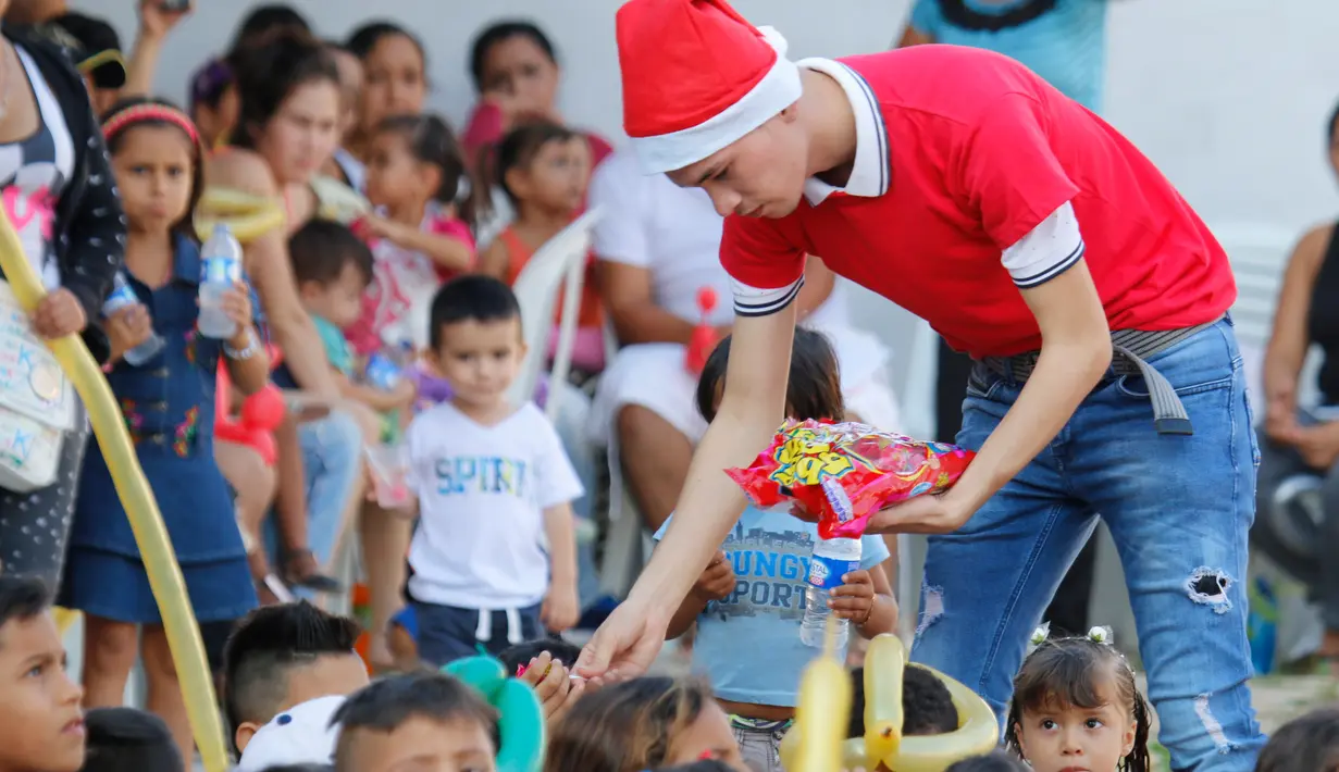 Seorang pegawai Kementerian Luar Negeri Kolombia memberikan hadiah kepada anak-anak imigran Venezuela di Cucuta, Kolombia, di perbatasan dengan Venezuela, pada Malam Natal (24/12). (AFP Photo/Schneyder Mendoza)