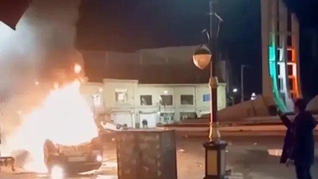 Cuplikan gambar dari video yang dirilis pada Jumat (9/1/2026) oleh televisi pemerintah Iran memperlihatkan seorang pria memegang sebuah perangkat untuk mendokumentasikan kendaraan yang terbakar selama aksi protes massal pada malam hari di Zanjan, Iran.