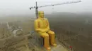 Sebuah Crane saat beroperasi di sebelah patung Presiden pertama Cina, Mao Zedong saat proses penyelesaian pembangunannya di ladang Desa Tongxu, Henan, Cina (4/1). Patung ini memiliki tinggi 36,6 meter dan dilapisi cat emas. (Reuters/Stringer)