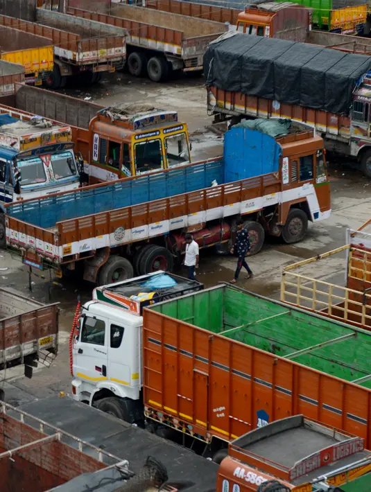 Dua pria berjalan melewati truk-truk yang diparkir di sebuah terminal di Chennai (19/9/2019). Layanan transportasi darat menyerukan pemogokan satu hari untuk memprotes kenaikan pinalti di bawah Undang-undang Kendaraan Bermotor (Amandemen) yang baru. (AFP Photo/Arun Sankar)