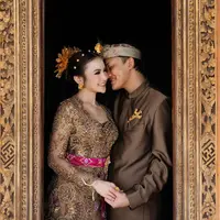 Sambil berpegang tangan mesra, Rizky Febian dan Mahalini tampil mengenakan busana adat Bali warna cokelat yang serasi. [@axioo]