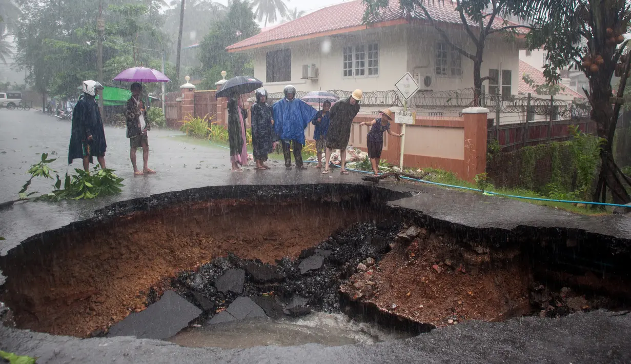 Orang-orang melihat lubang besar di jalan yang disebabkan setelah banjir di Mawlamyein, negara bagian Mon (9/8/2019). Hujan lebat yang menguyur Myanmar membuat banjir di beberapa wilayah dan memaksa puluhan ribu warga diungsikan dari rumah mereka. (AFP Photo/Chit Ko Lin)