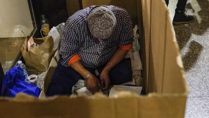 Tunawisma bersiap untuk makan makanan gratis dari Progetto Arca Onlus di dalam karton darurat di Milan, Italia utara, 27 November 2020. Tidak ada tempat di Italia yang kemiskinan lebih jelas daripada di Lombardy, wilayah utara yang sempat menjadi episentrum penularan COVID-19. (AP Photo/Luca Bruno)