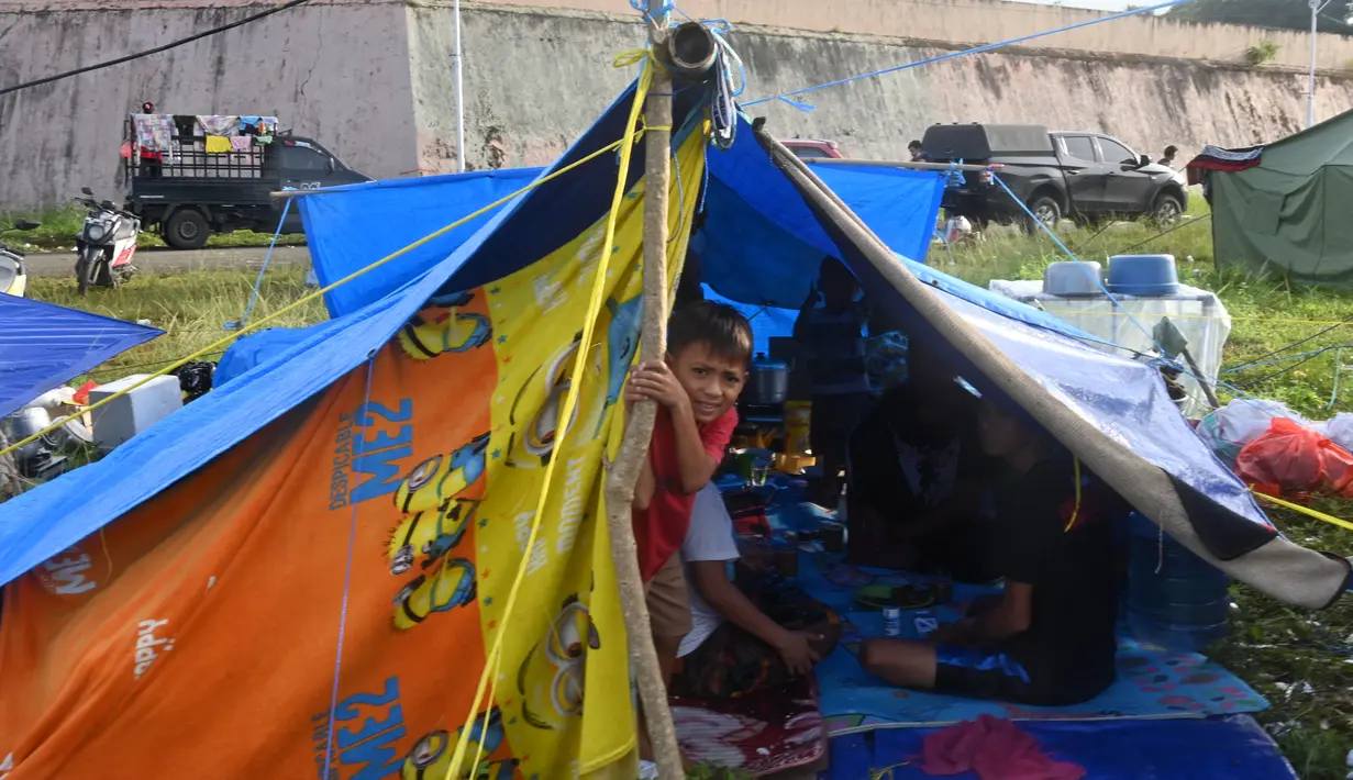 Seorang anak laki-laki mengintip dari tenda ketika orang-orang yang terkena gempa tinggal di kamp sementara setelah gempa berkekuatan 6,2 di Mamuju, Senin (18/1/2021). Ratusan jiwa telah mengungsi di sejumlah posko pengungsian karena rumah mereka rusak akibat gempa. (AFP/Adek Berry)