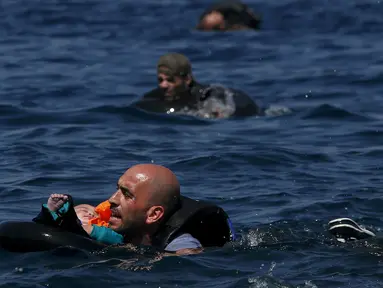 Seorang pengungsi Suriah membawa bayi menggunakan pelampung dan berenang menuju pantai setelah perahu yang ditumpangi bocor sekitar 100 m sebelum mencapai pulau Lesbon, Yunani, Minggu (13/09/2015). (REUTERS/Alkis Konstantinidis) 