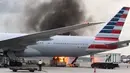 Api berkobar dengan asap hitam naik dekat lambung pesawat American Airlines yang terparkir di landasan Bandara Internasional Hong Kong, Senin (9/10). Api nyaris membakar bagian perut pesawat di antara sayap kanan dan sayap ekor. (U87 via AP)
