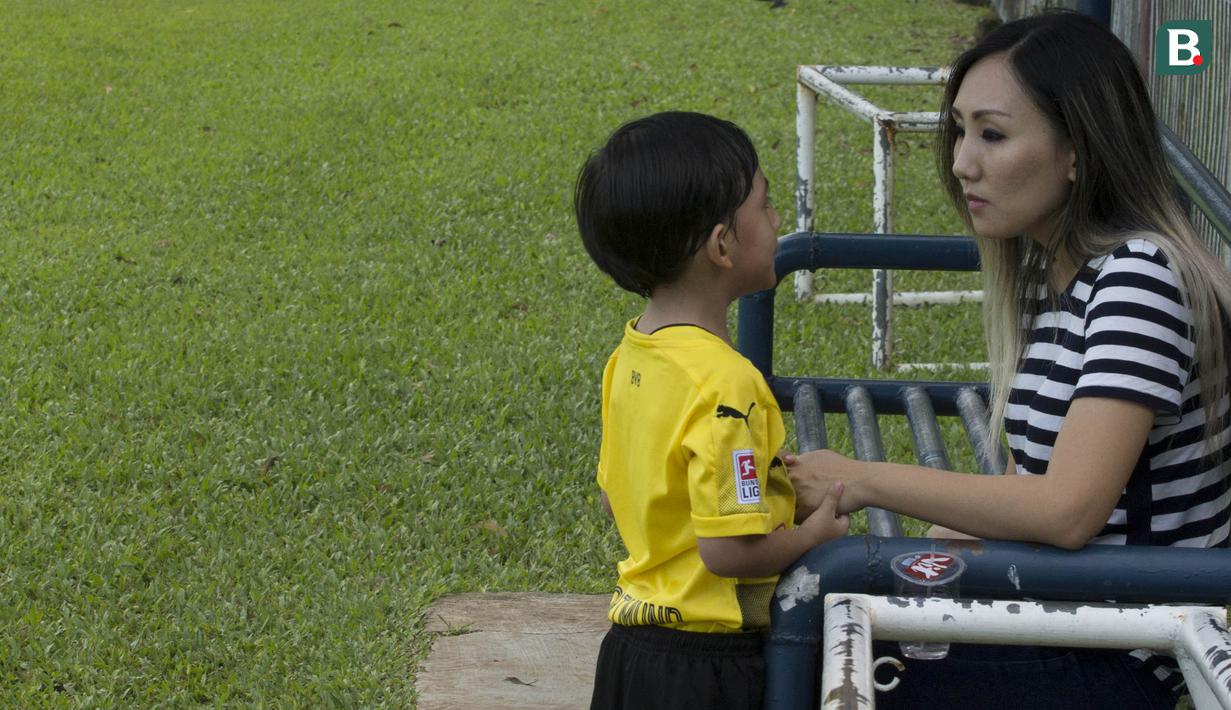 Anak dari Stefano Teco, yang bernama Romario, bersama ibunya, Miranda, saat latihan Persija Jakarta di Lapangan Sutasoma, Jakarta, Minggu (25/2/2018). Ketika ayahnya bekerja sang anak asyik bermain sepak bola. (Bola.com/Aspirilla Dwi Adha)