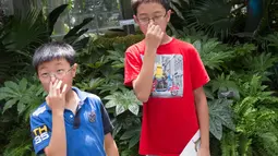 Dua anak dari Toronto, Kanada, menutup hidung mereka saat melihat bunga bangkai raksasa Titan Arum di Botanic Garden, Washington, Amerika Serikat, Senin (2/8). Bunga bangkai raksasa dari Sumatera ini tak lama lagi akan mekar sempurna. (Chris KLEPONIS/AFP)