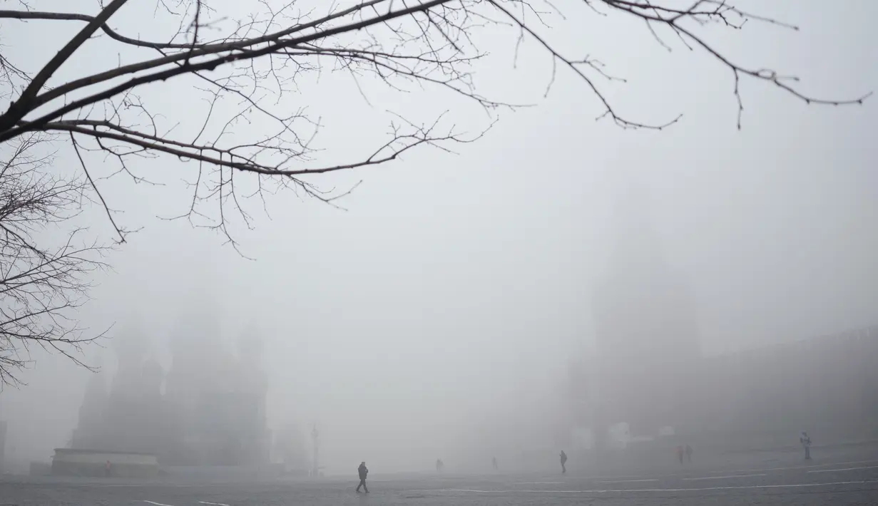 Orang-orang berjalan di Lapangan Merah, dengan Menara Spasskaya, kanan, dan Katedral St. Basil terlihat melalui kabut di Moskow, Rusia, Selasa (2/11/2021).  Kabut tebal menyelimuti ibu kota Rusia pada Selasa, menyebabkan banyak penundaan penerbangan di bandara Moskow. (AP Photo/Pavel Golovkin)