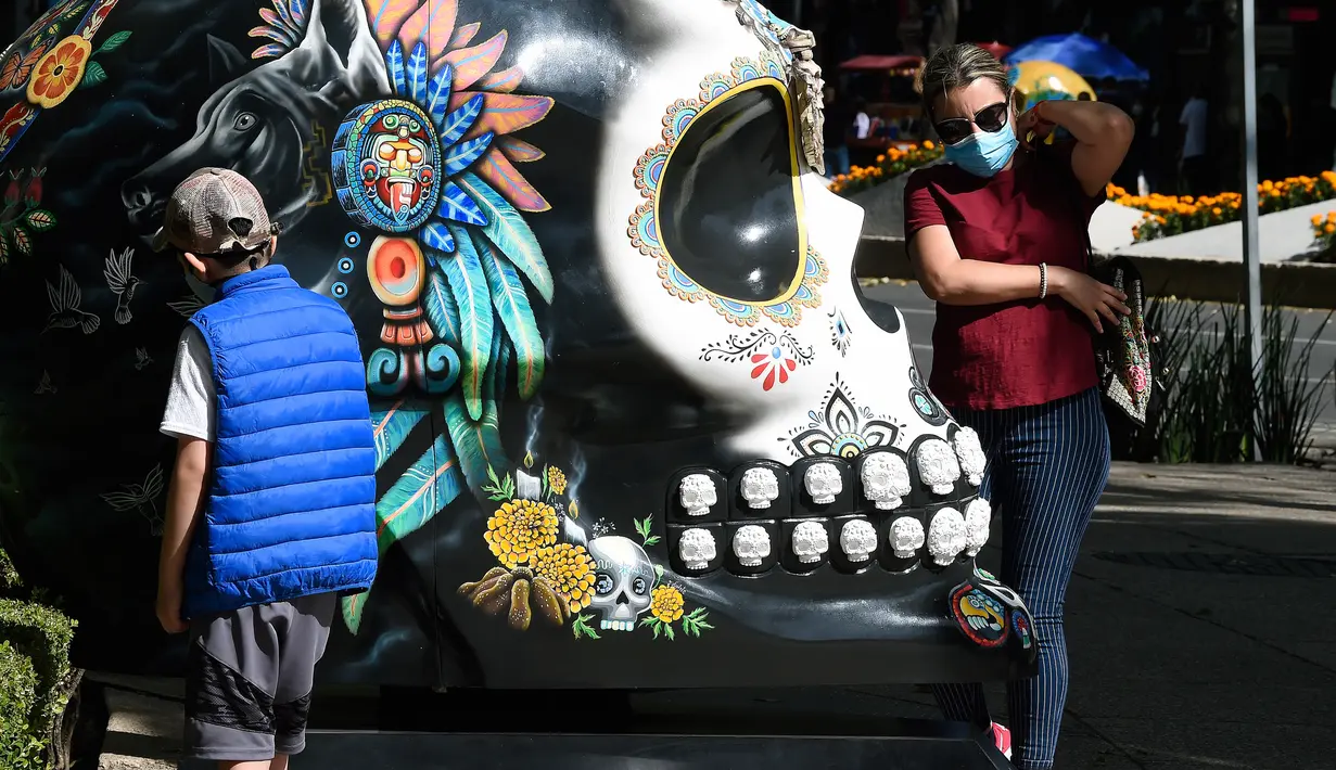 Seorang anak dan perempuan berada di samping tengkorak yang dihias selama pameran edisi keempat "Mexicraneos" (Mexisculls) di Reforma Avenue, Mexico City pada 23 Oktober 2020. Pameran itu karya seniman dari berbagai bagian negara Meksiko, juga Amerika Serikat dan Venezuela. (ALFREDO ESTRELLA/AFP)