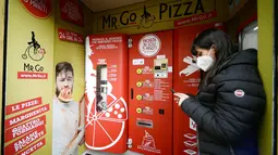 Seorang wanita menunggu pesanannya di mesin penjual pizza otomatis, yang pertama dari jenisnya di pusat kota Roma, pada 29 April 2021. Mesin penjual otomatis ini mampu menguleni adonan, membumbui, memasak, dan menyajikan pizza dalam kotak karton hanya dalam waktu tiga menit. (Filippo MONTEFORTE/AFP)