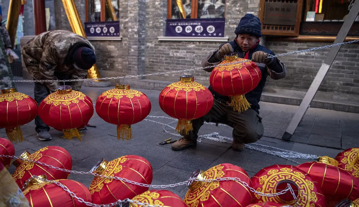 Para pekerja memasang lentera tradisional Tiongkok di sepanjang gang menjelang Tahun Baru Imlek di Beijing, China, 2 Februari 2021. Imlek tahun ini jatuh pada tanggal 12 Februari 2021. (NOEL CELIS/AFP)