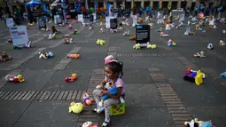 Seorang anak duduk bersama ratusan boneka saat menggelar aksi memprotes penganiayaan terhadap anak sekaligus meningkatkan kesadaran akan tanggung jawab dalam perlindungan anak di Alun-alun Bolivar, Bogota, Kolombia (20/11). (AFP Photo/Raul Arboleda)