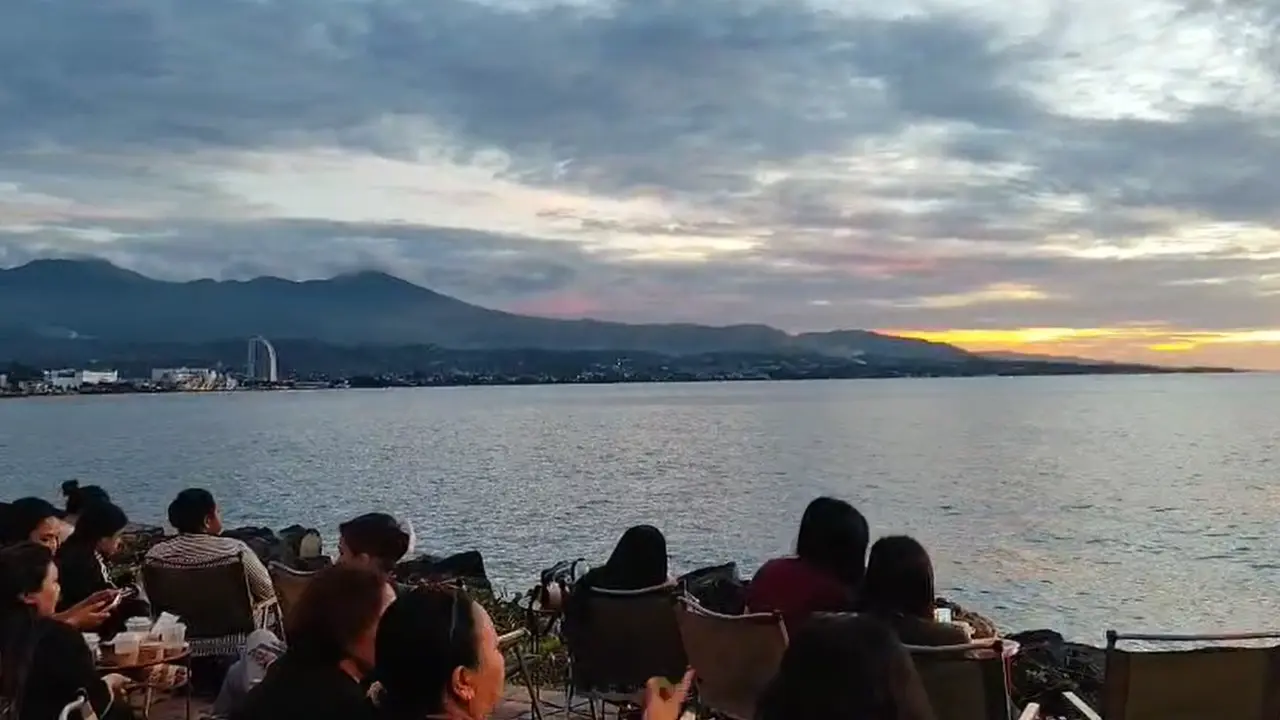 Warga duduk duduk menikmati matahari terbenam di kawasan Megamas, Manado.