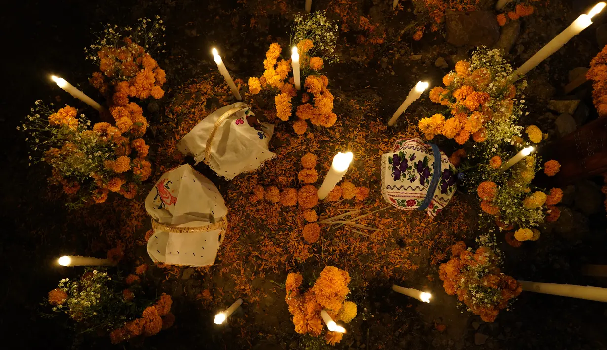 Bunga, persembahan makanan, dan lilin menghiasi makam pada perayaan Hari Kematian di pemakaman Arocutin, Michoacan, Meksiko, 1 November 2021. Pada Hari Kematian, kerabat menghabiskan malam di samping makam orang yang mereka cintai. (AP Photo/Eduardo Verdugo)