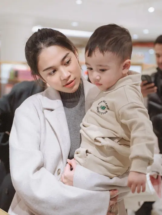Bertemu dengan Rayyanza, putra Raffi Ahmad-Nagita Slavina, Azizah terlihat menawan dengan long coat warna beige dan turtleneck warna abu-abunya. [@azizahsalsha_]