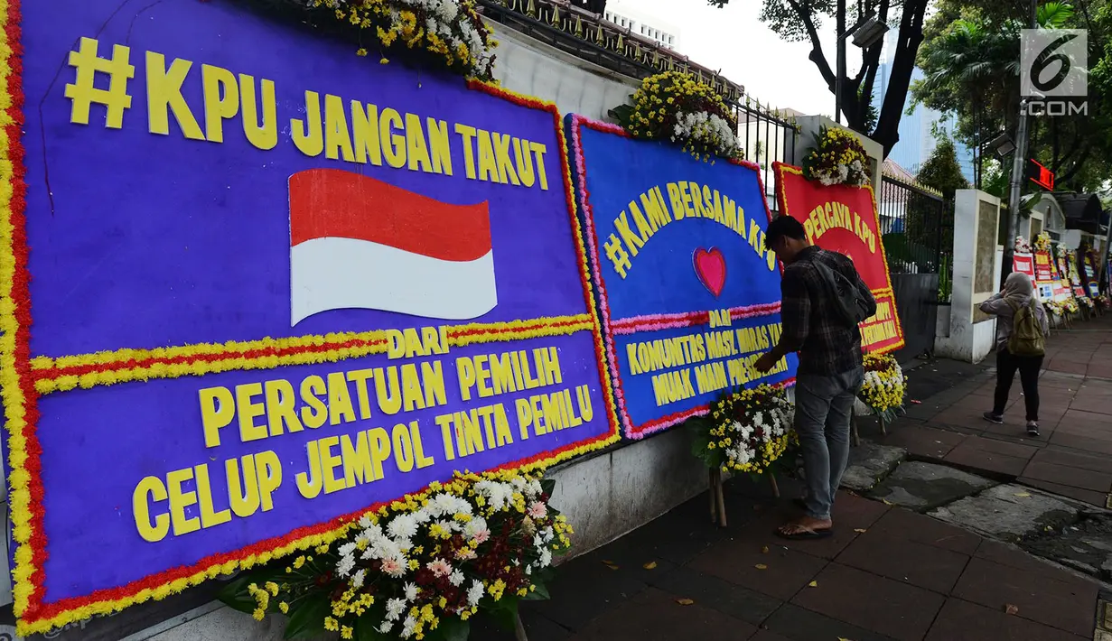 Warga melihat karangan bunga yang ada di Gedung Komisi Pemilihan Umum (KPU), Jakarta, Sabtu (20/4). Karangan bunga tersebut merupakan dukungan masyarakat kepada KPU untuk terus berkerja maksimal dalam menghitung suara Pilpres 2019. (merdeka.com/Imam Buhori)