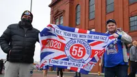 Dua fans Glasgow Rangers membentangkan bendera klub di luar Ibrox Stadium (7/3/2021) untuk merayakan keberhasilan tim kesayangan mereka merebut gelar Liga Utama Skotlandia setelah memimpin 20 poin dari saingan terdekat, Glasgow Celtic. (AFP/Andy Buchanan)