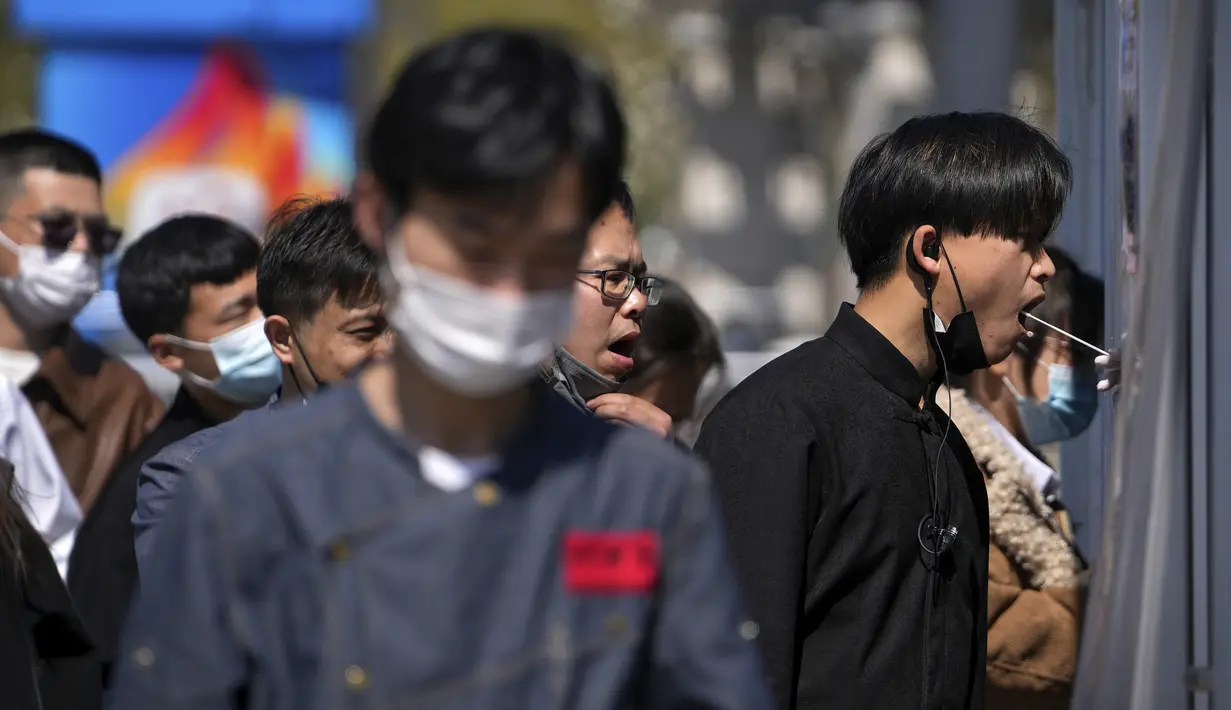 Para pekerja yang mengenakan masker antre mengambil swab tenggorokan di tempat pengujian virus corona di Beijing, Minggu (3/4/2022). Kasus COVID-19 di kota terbesar di China, Shanghai, masih meningkat saat jutaan orang tetap terisolasi di rumah di bawah lockdown besar-besaran. (AP Photo/Andy Wong)
