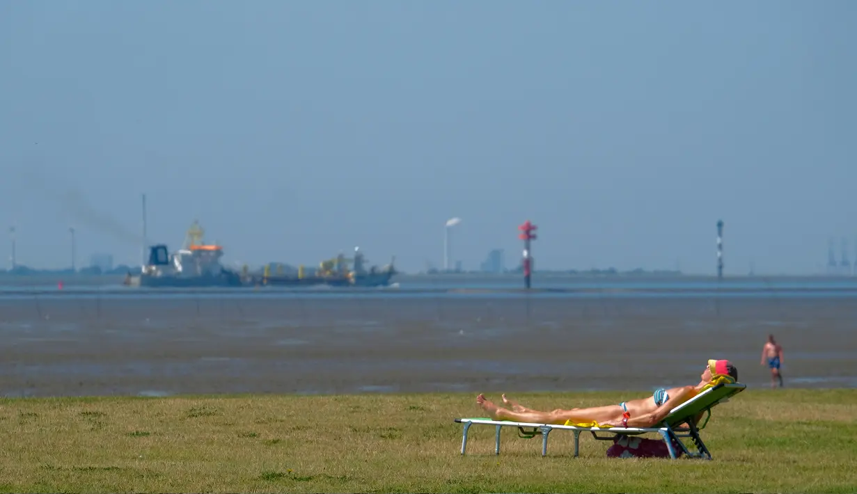 Seorang wanita berjemur ketika kapal kargo menuju Laut Utara saat suhu mencapai 34 derajat Celcius di dekat pantai Laut Utara di Wremen, Jerman barat (24/7/2019). (AFP Photo/Patrik Stollarz)