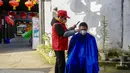 Seorang barber sukarelawan memotong rambut seorang pria di sebuah permukiman di Kota Chongqing, China barat daya, pada 16 Februari 2020. Sejak merebaknya virus corona COVID-19, sebagian besar tempat potong rambut telah ditutup. (Xinhua/Liu Chan)