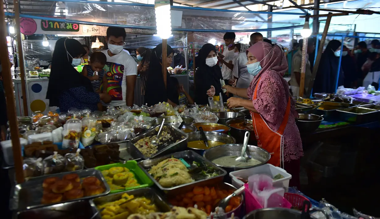 Orang-orang memakai masker di kios-kios yang dikelilingi oleh pelindung plastik di pasar, sebagai bagian dari upaya untuk menghentikan penyebaran virus corona Covid-19, selama bulan suci Ramadhan di provinsi selatan Thailand, Narathiwat (17/4/2021). (AFP/Madaree Tohlala)