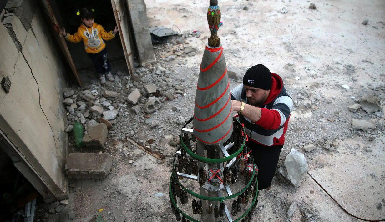 Akram Abu al-Foz menghias sebuah pohon Natal buatannya di wilayah yang dikuasai oposisi di Douma, Suriah, Jumat (23/12). Pohon Natal itu terbuat dari sisa-sisa amunisi perang antara pemberontak dan pasukan rezim Bashar Al Assad. .(REUTERS/Bassam Khabieh)