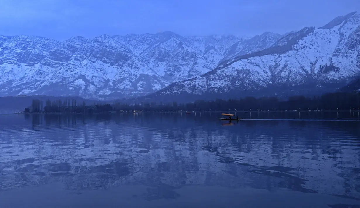 Orang-orang menikmati perjalanan dengan perahu dengan latar belakang pegunungan yang tertutup salju di danau Dal di Srinagar (11/1/2022). Danau Dal di Kashmir bisa dibiland danau terindah di kaki Pegunungan Himalaya. (AFP/Tauseef Mustafa)