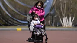 Seorang perempuan mengenakan masker wajah membawa anaknya menuju sebuah taman, di Beijing, Minggu (3/4/2022). Kasus COVID-19 di kota terbesar di China, Shanghai, masih meningkat saat jutaan orang tetap terisolasi di rumah di bawah lockdown besar-besaran. (AP Photo/Andy Wong)