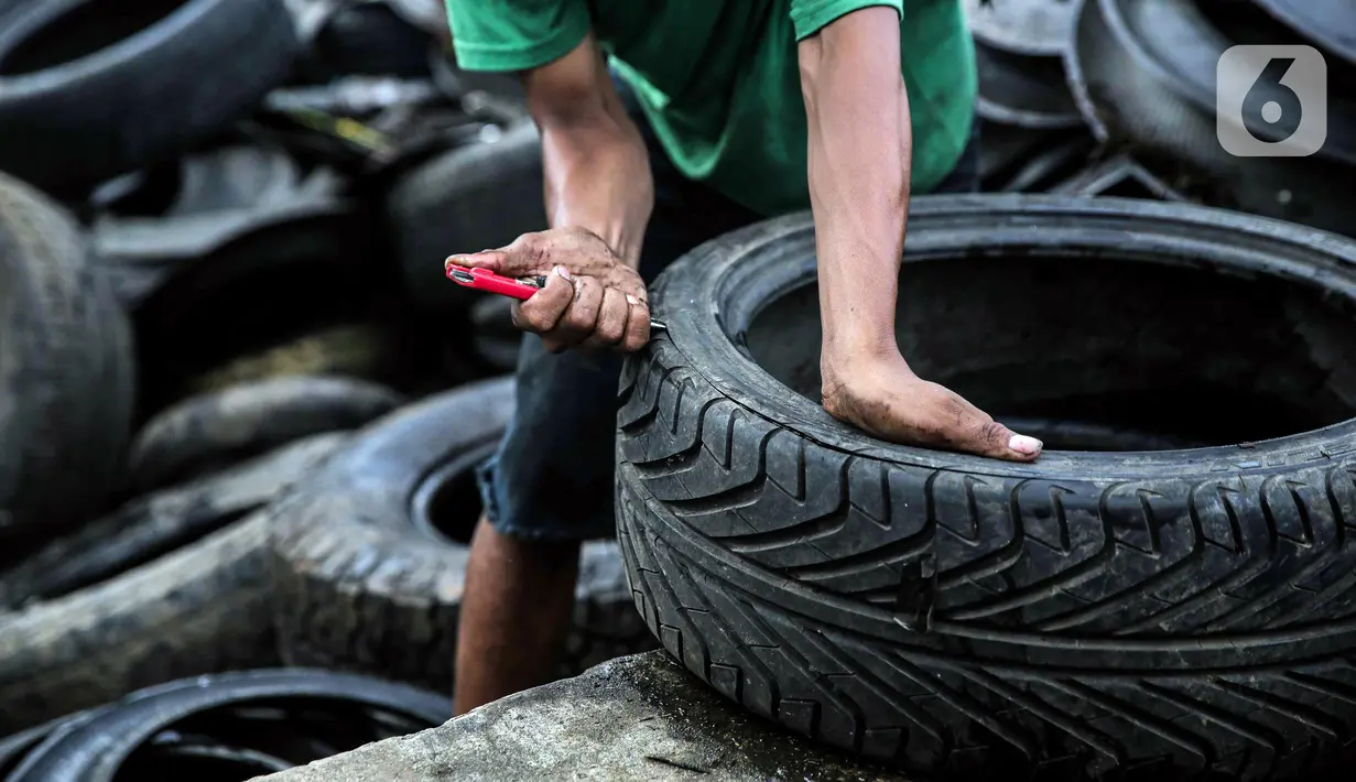 Pekerja memotong ban mobil bekas di kawasan Petamburan, Jakarta, Minggu (12/12/2021). Ban bekas ini nantinya akan dilebur untuk dijadikan minyak serta bahan baku pembuatan aspal. (Liputan6.com/Faizal Fanani)