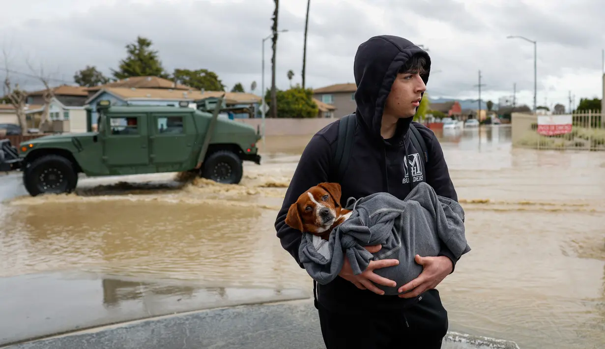 Esteban Sepulveda menggendong anjingnya Milo saat meninggalkan rumahnya di Lembah Pajaro, California, Amerika Serikat, 12 Maret 2023. Di seluruh Monterey County, lebih dari 8.500 orang pada hari Sabtu (11/3) diperintahkan untuk segera meninggalkan daerah itu, termasuk sekitar 1.700 pekerja pertanian yang kebanyakan berasal dari Amerika Latin. (Shae Hammond/Bay Area News Group via AP)