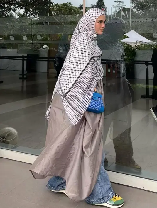 Kali ini ia tampil lebih cerah dengan kerudung panjang bermotif shemagh hitam putih dipadukan abaya coklat serta celana denim dan sneakersnya.  [@siviazizah]