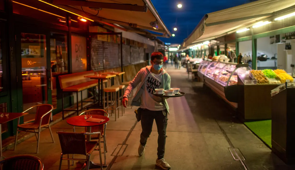 Pramusaji membersihkan makanan dari meja, yang biasanya dilakukan oleh pengujung, di pasar Naschmark di Wina, Austria pada 5 Oktober 2020. Naschmarkt adalah pasar tertua, terbesar, dan terpopuler di Wina kini sepi pengunjung akibat pandemi corona COVID-19. (JOE KLAMAR / AFP)