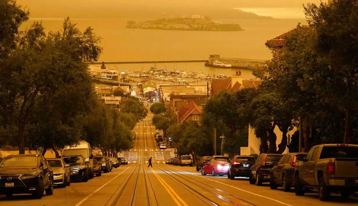 Seorang pria melintasi Hyde Street dengan Pulau Alcatraz dan Fisherman's Wharf terlihat pada latar belakang di San Francisco, Amerika Serikat, Rabu (9/9/2020). Kebakaran hutan di seluruh Barat mengakibatkan langit San Francisco hingga Seattle berwarna oranye yang menakutkan. (AP Photo/Eric Risberg)