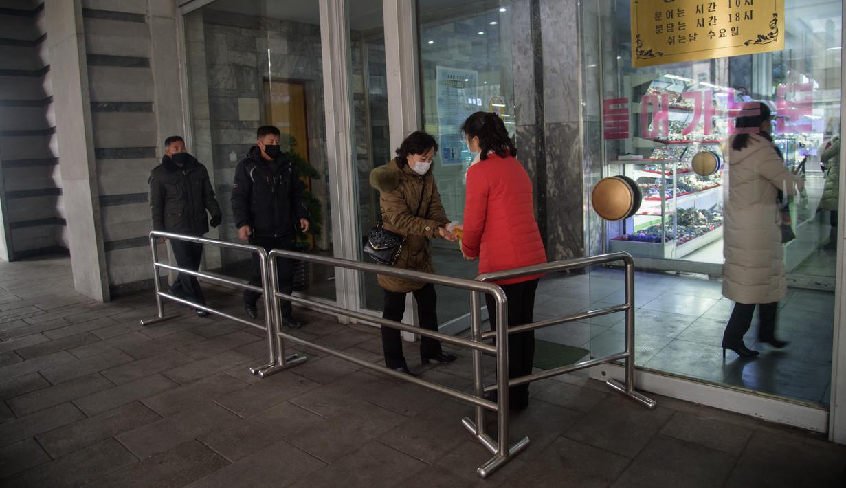 Petugas menyemprotkan sanitizer ke pengunjung di dalam Pyongyang Department Store No. 1, Korea Utara (28/12/2020). Meski Korea Utara melaporkan nol kasus Covid-19, pemerintahan Pyongyang tetap menerapkan standar protokol kesehatan guna mencegah penyebaran Covid-19. (AFP/Kim Won Jin)