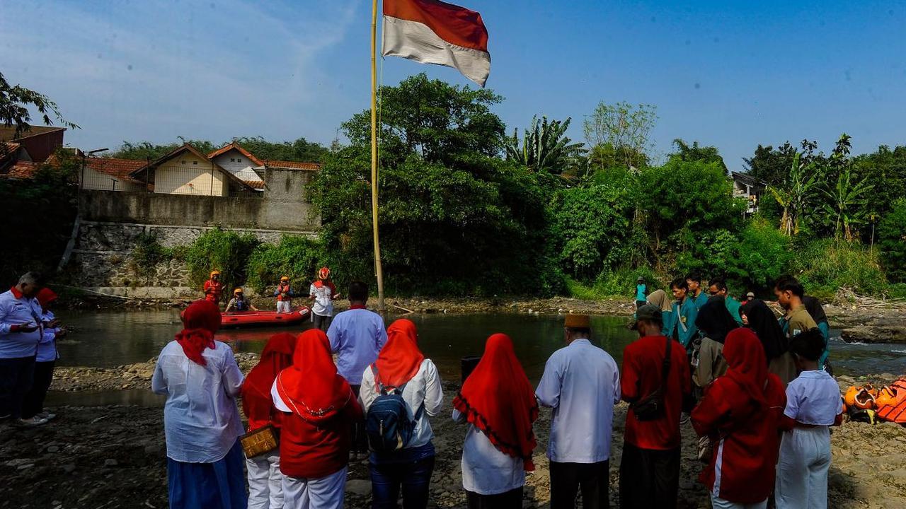 Warga RW 07 saat melakukan pengibaran bendera merah putih pada aliran Sungai Ciliwung yang mengering akibat kemarau panjang di Kedung Halang.