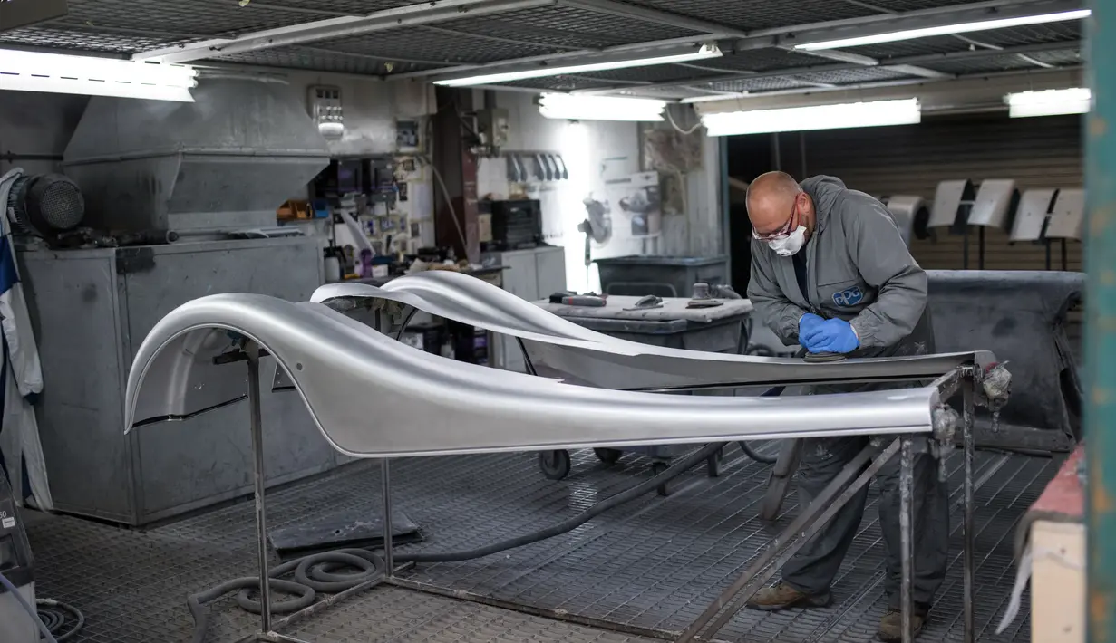 Pekerja memoles elemen aluminium dengan cat yang merupakan bagian body mobil klasik yang dibuat di Malvern, Birmingham, Inggris (13/8/2019).  Bahan yang digunakan untuk memproduksi mobil klasik ini memakai tiga elemen inti yakni kayu ash, aluminium dan kulit. (AFP Photo/Oli Scarff)