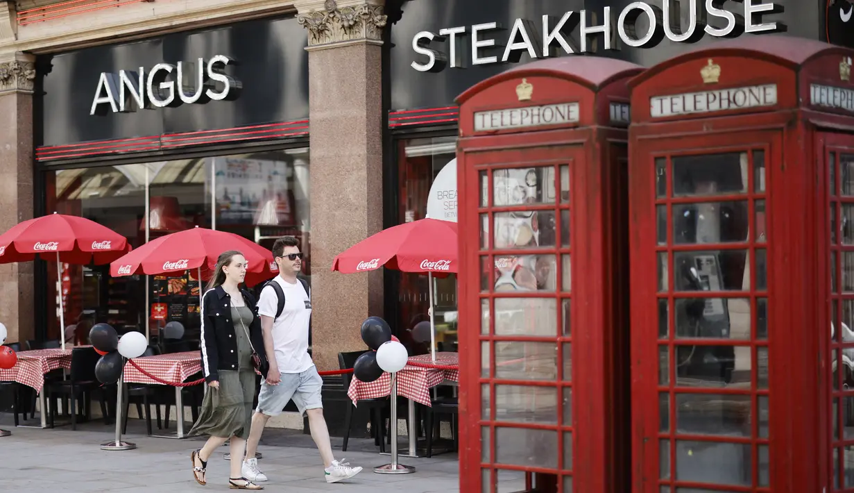 Sepasang kekasih berjalan melewati sebuah restoran di pusat kota London pada Kamis (3/6/2021). Pemerintah Inggris belum bisa memastikan akan sepenuhnya mencabut lockdown yang berakhir pada 21 Juni nanti meski kasus Covid-19 mengalami tren penurunan. (Tolga Akmen/AFP)