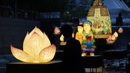 Seorang pengunjung yang mengenakan masker untuk membantu mengekang penyebaran virus corona mengambil foto di dekat lentera yang dipajang untuk merayakan ulang tahun Buddha yang akan datang pada 8 Mei, di aliran umum di Seoul, Korea Selatan, Selasa, 26 April 2022. (AP Photo /Lee Jin-man)