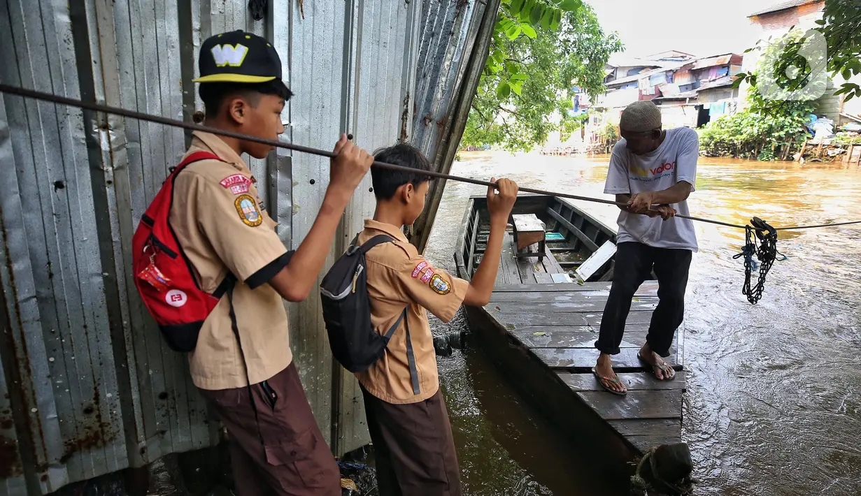 Dua orang pelajar bersiap naik perahu eretan untuk menyeberangi kali Ciliwung di area Manggarai, Jakarta, Rabu (14/5/2025). (detikai.com/Angga Yuniar)